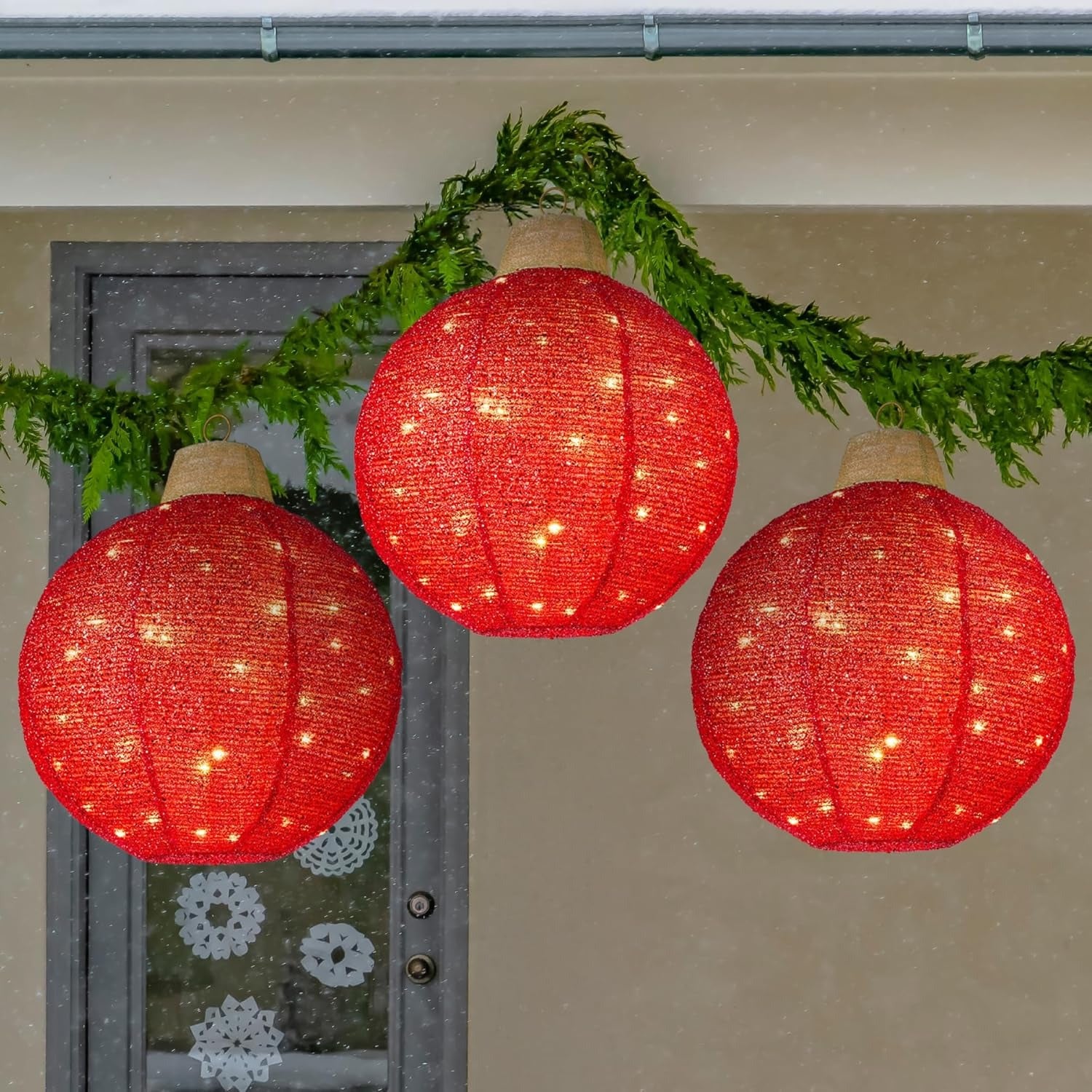 Three red LED lanterns hanging on a string with greenery against a door with snowflake decorations.